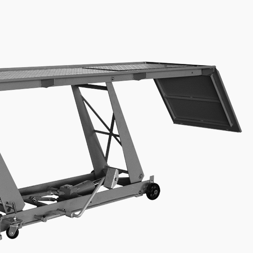 Mobiler Scherenhubtisch aus Metall in grauer Ausführung mit hydraulischem Hubmechanismus. Die rechteckige Arbeitsplattform besteht aus einem rutschhemmenden Gitter, an einer Stirnseite ist eine klappbare Auffahrrampe angebracht. Unter der Plattform sind Scherenarme, Hydraulikzylinder, Transportrollen und ein Fußhebel zur Bedienung sichtbar. Freigestellt vor weißem Hintergrund.