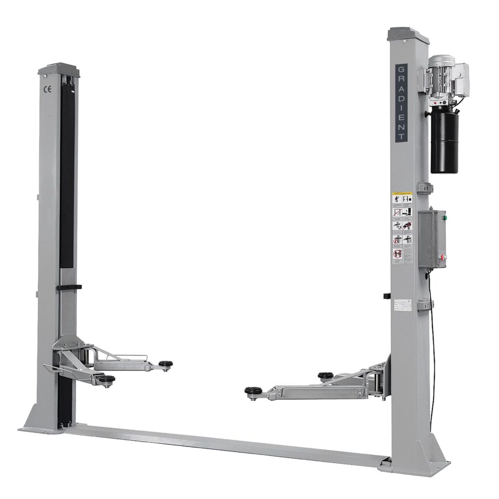 Freistehende Kfz-Zweisäulenhebebühne in Frontansicht mit zwei grauen Säulen, integrierter Hydraulikeinheit und schwenkbaren Tragar­men. Die Bühne verfügt über eine Bodenquertraverse, höhenverstellbare Aufnahmeteller und eine Steuereinheit an der rechten Säule, weißer Hintergrund.